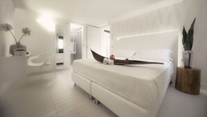 A modern bedroom with a large bed, a white chair, and a wooden side table. - Q Hotel (Rimini)