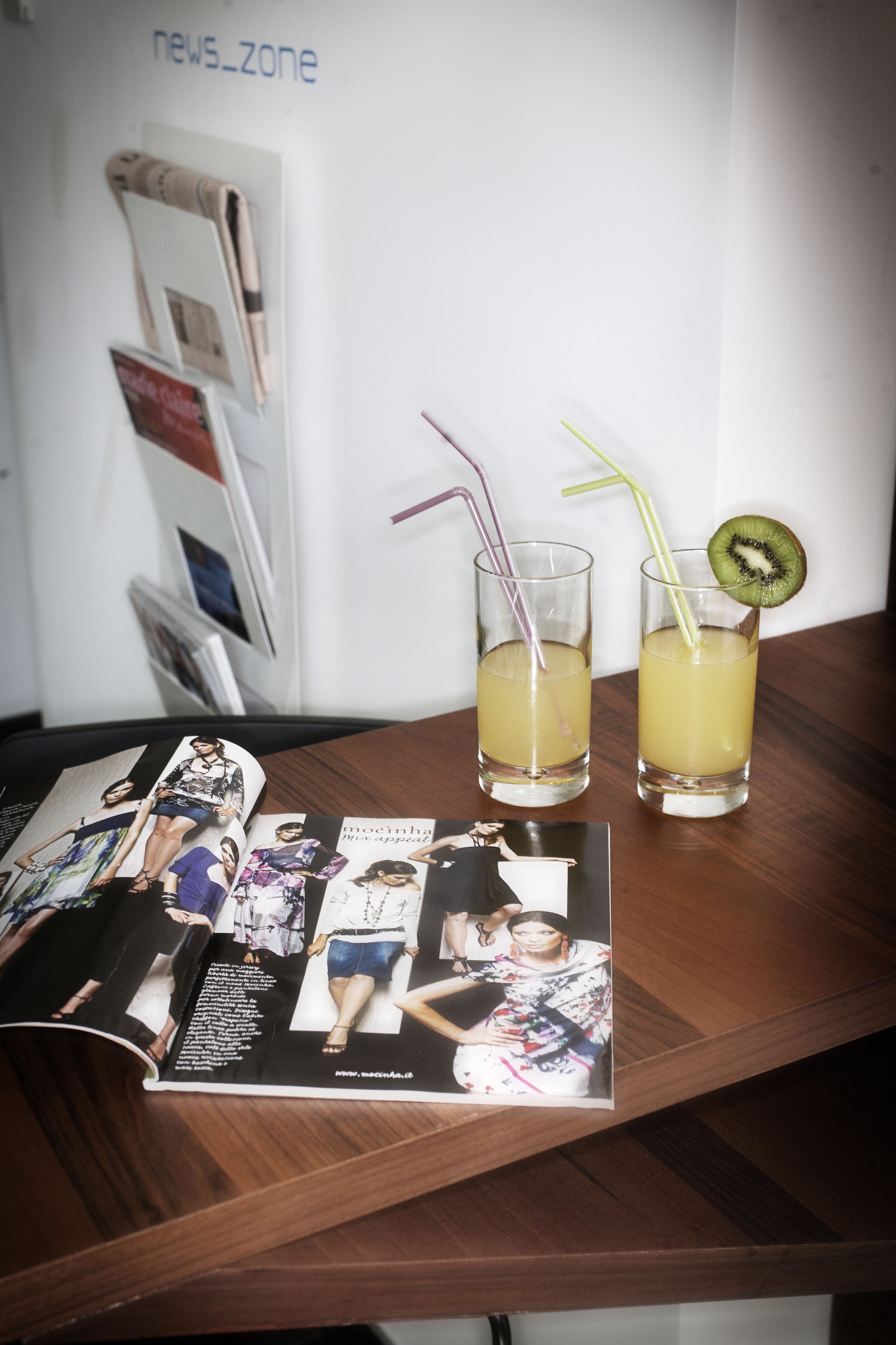 Una revista sobre una mesa con dos vasos de una bebida amarilla, uno con pajita y el otro con una rodaja de kiwi.