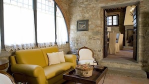 A cozy room with a stone wall, a yellow sofa, a white armchair, and a fireplace. - Relais Colline San Biagio (Carmignano)