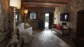 A rustic room with stone walls, a white sofa, a wooden bench, and a lamp. - Relais Colline San Biagio (Carmignano)