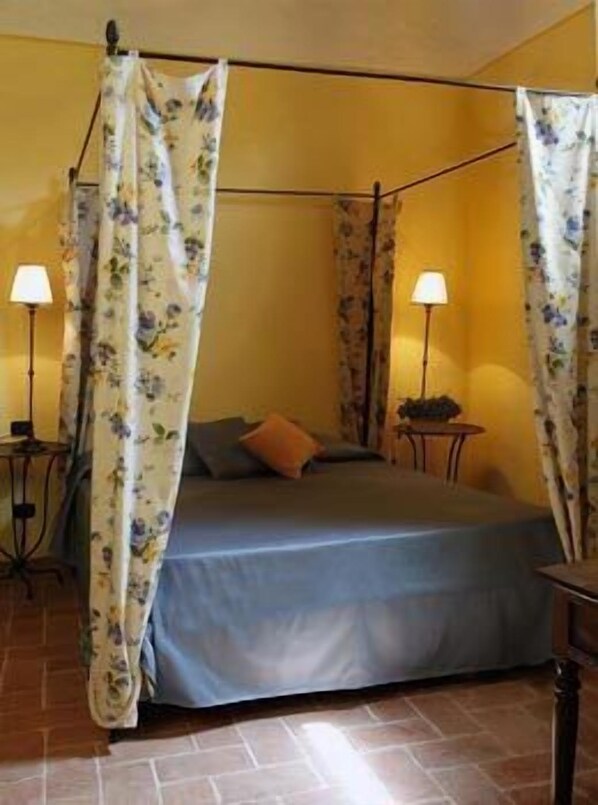 A room with a four-poster bed, two bedside lamps, and a floral curtain.