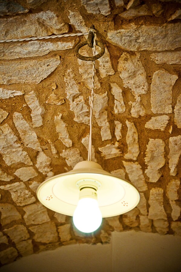 Una lámpara colgante con pantalla blanca suspendida de una cadena frente a una pared de piedra texturizada.