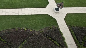 Un jardin aménagé avec une allée centrale pavée, entouré de pelouses verdoyantes et de parterres recouverts d’une couche de paillis sombre.