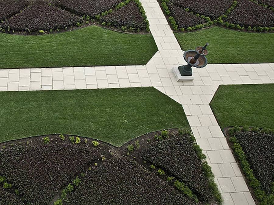 Un jardín ajardinado con un sendero pavimentado central, rodeado de césped verde y bancales con acolchado oscuro.