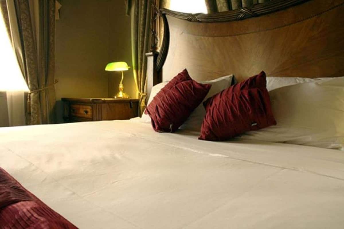 A neatly made bed with white linens and two red pillows, a wooden headboard, and a nightstand with a lamp.