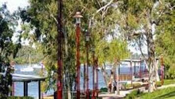 A pathway lined with red lampposts and trees, leading to a waterfront area with a gazebo.