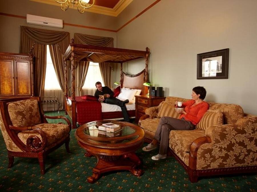 A traditional room with a four-poster bed, a sitting area with a sofa and armchairs, and a round coffee table.