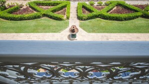 Un balcon donnant sur un jardin magnifiquement entretenu, avec des haies aux formes géométriques et une fontaine centrale.
