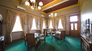 Une salle à manger avec un tapis à motifs verts, des meubles en bois et un lustre.