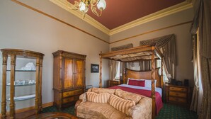 Une chambre à coucher avec un lit à baldaquin, une armoire en bois, un meuble vitré et un sol recouvert d’une moquette verte.