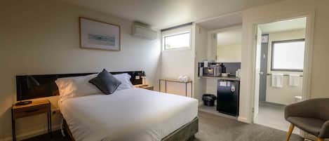 A hotel room with a bed, bedside tables, a desk, a chair, a kitchenette, and a bathroom.
