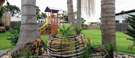 Un jardín con macetas circulares tejidas, un parque infantil y palmeras.