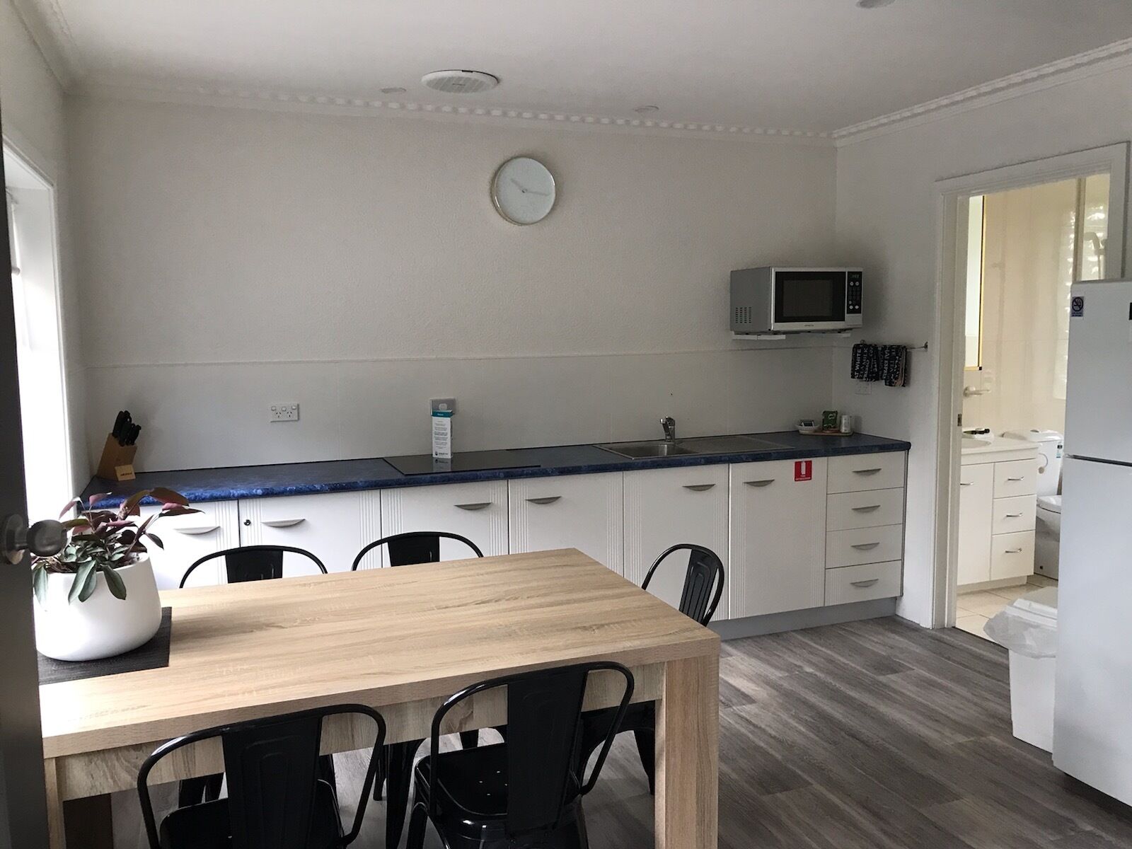 A modern kitchen with white cabinets, a wooden dining table, and black chairs.