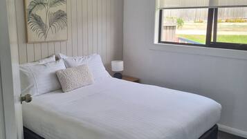 A bedroom with a bed, a ceiling fan, a window with a view of the outdoors, and a wall-mounted artwork.