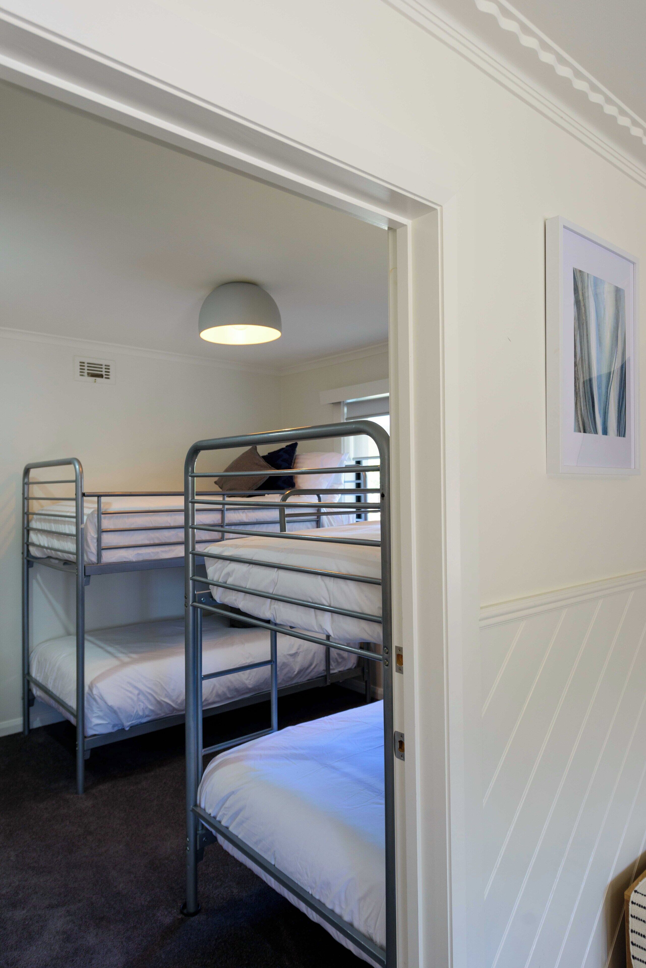 A room with bunk beds, a ceiling light, and a framed picture on the wall.