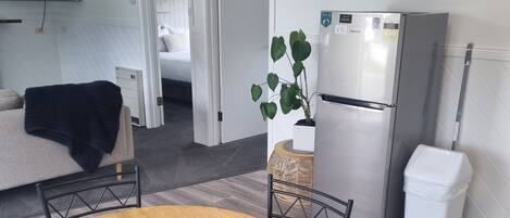 A compact kitchen with a refrigerator, a dining table with chairs, and a potted plant.