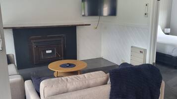 A modern living room with a sofa, a small round table, a flat-screen TV mounted on the wall, and a fireplace.