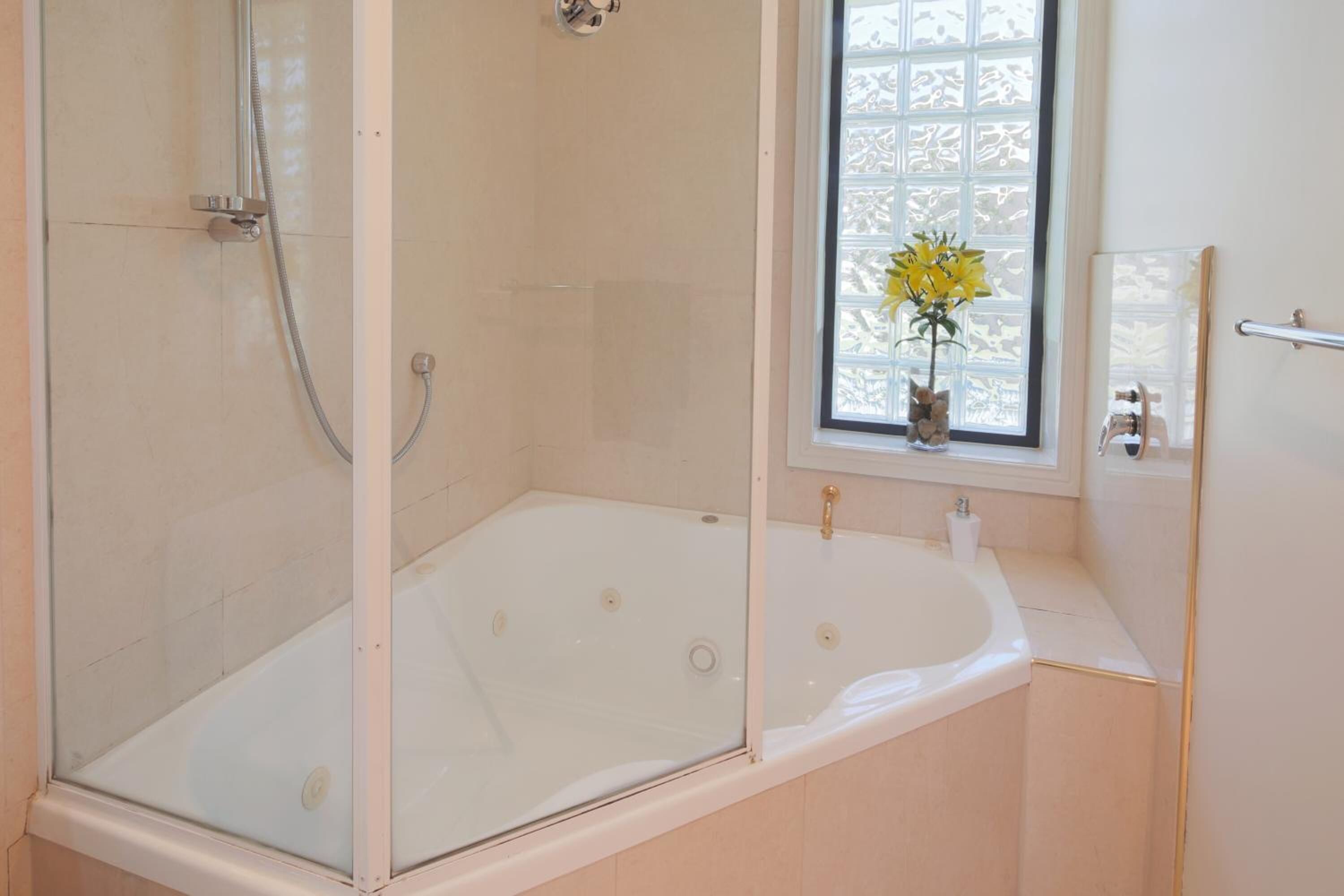 A bathroom with a glass-enclosed shower, a bathtub, and a window with a vase of flowers.