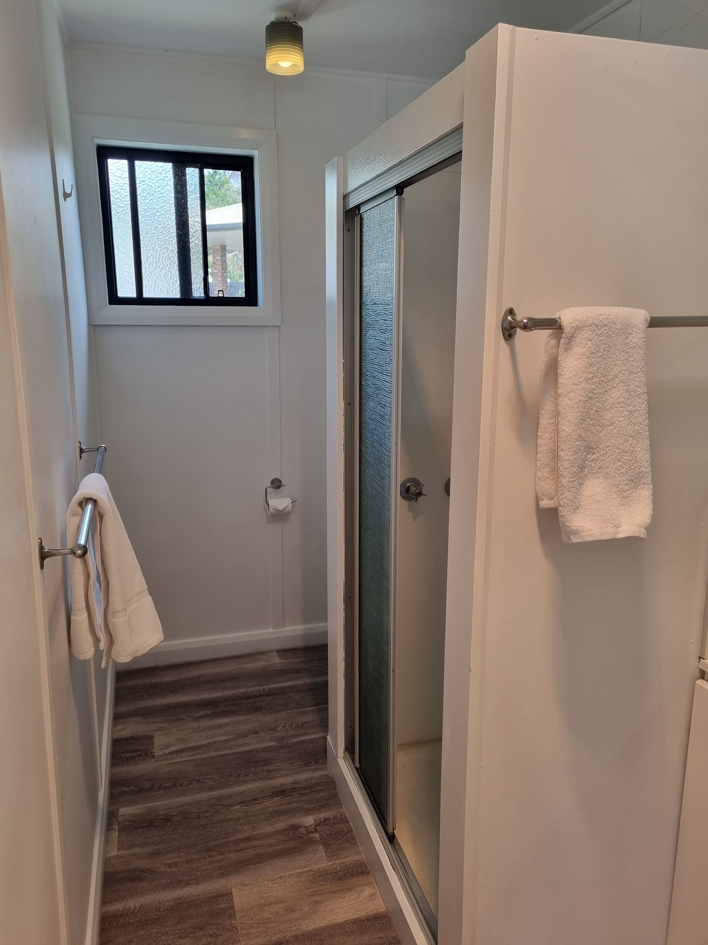 Un pasillo estrecho con suelo de madera, una puerta de vidrio y una ventana con barrotes.