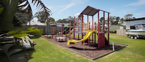 Une aire de jeux avec des toboggans et des structures d’escalade, entourée d’herbe et d’arbres.
