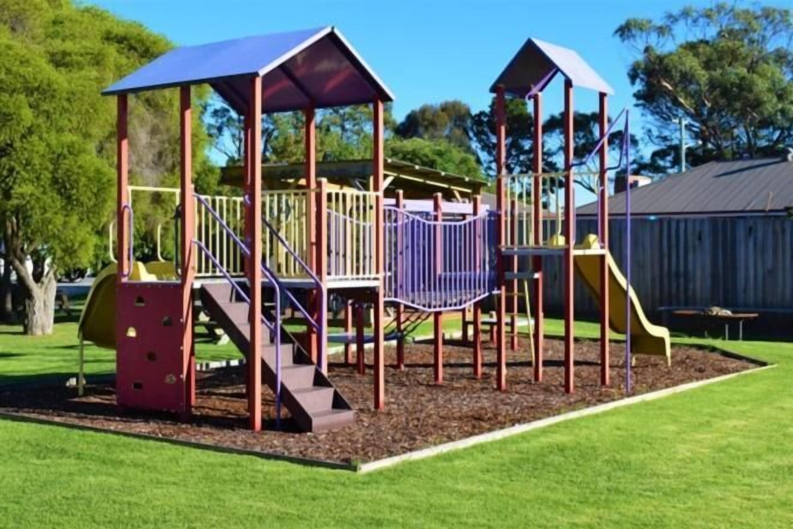 Ein Spielplatz mit einer Kletterkonstruktion, Rutschen und einem überdachten Spielbereich.