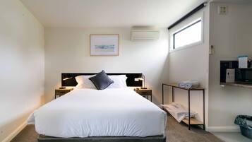 Una cama bien hecha en una habitación de hotel, con cabecera, mesitas de noche con lámparas, un cuadro enmarcado en la pared y una ventana con vistas.