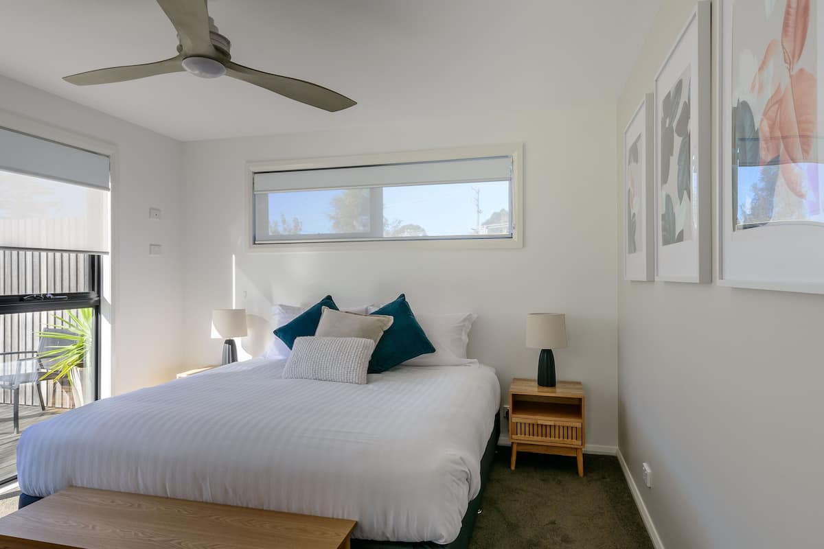 A hotel room with a bed, two bedside tables, a ceiling fan, a window, and a balcony with a chair and plant.