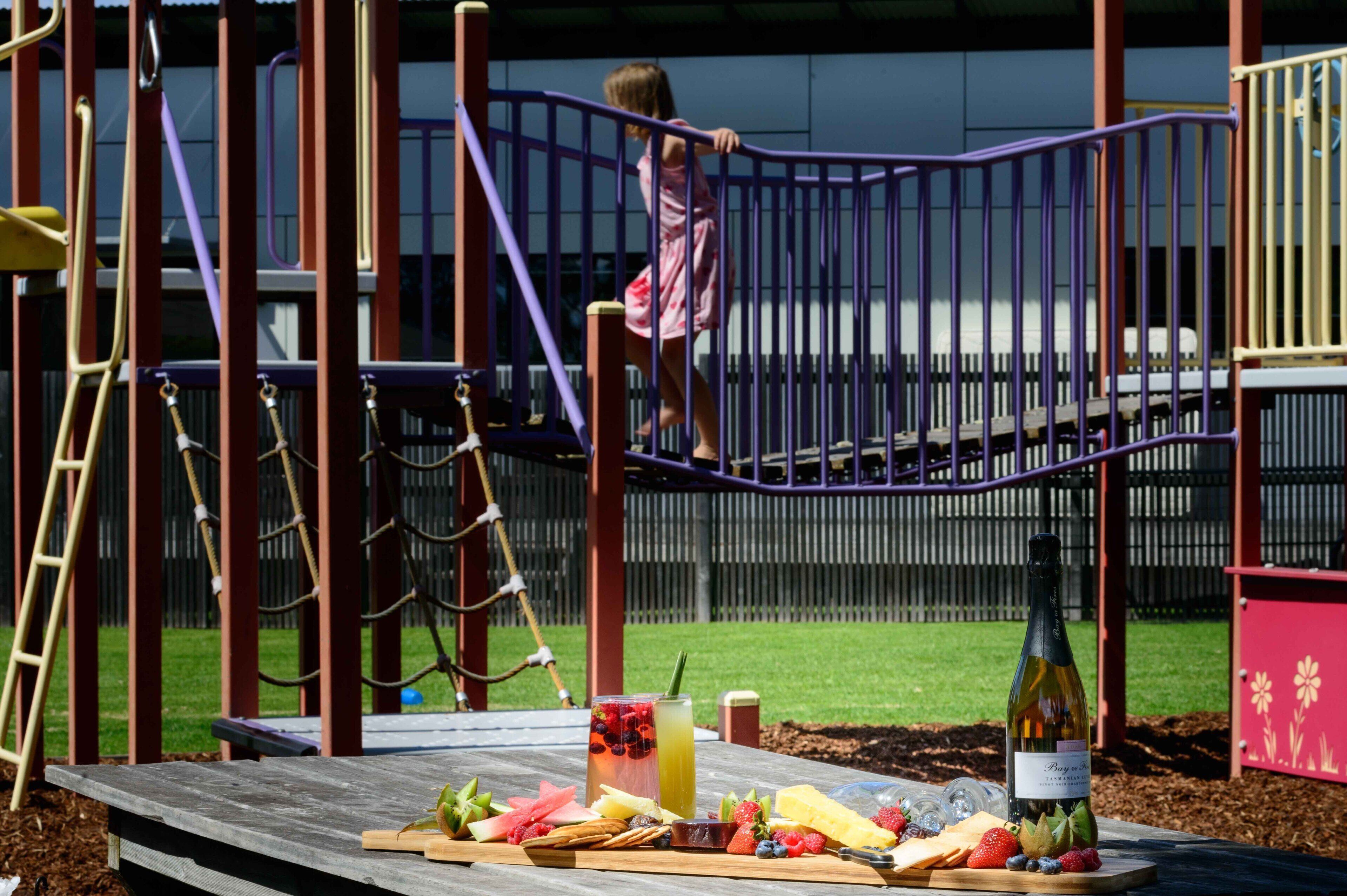 A playground with a wooden picnic table set up with food and drinks.
