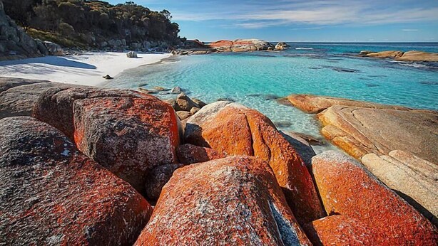 Un paisaje costero con rocas grandes, agua turquesa cristalina y una playa arenosa.