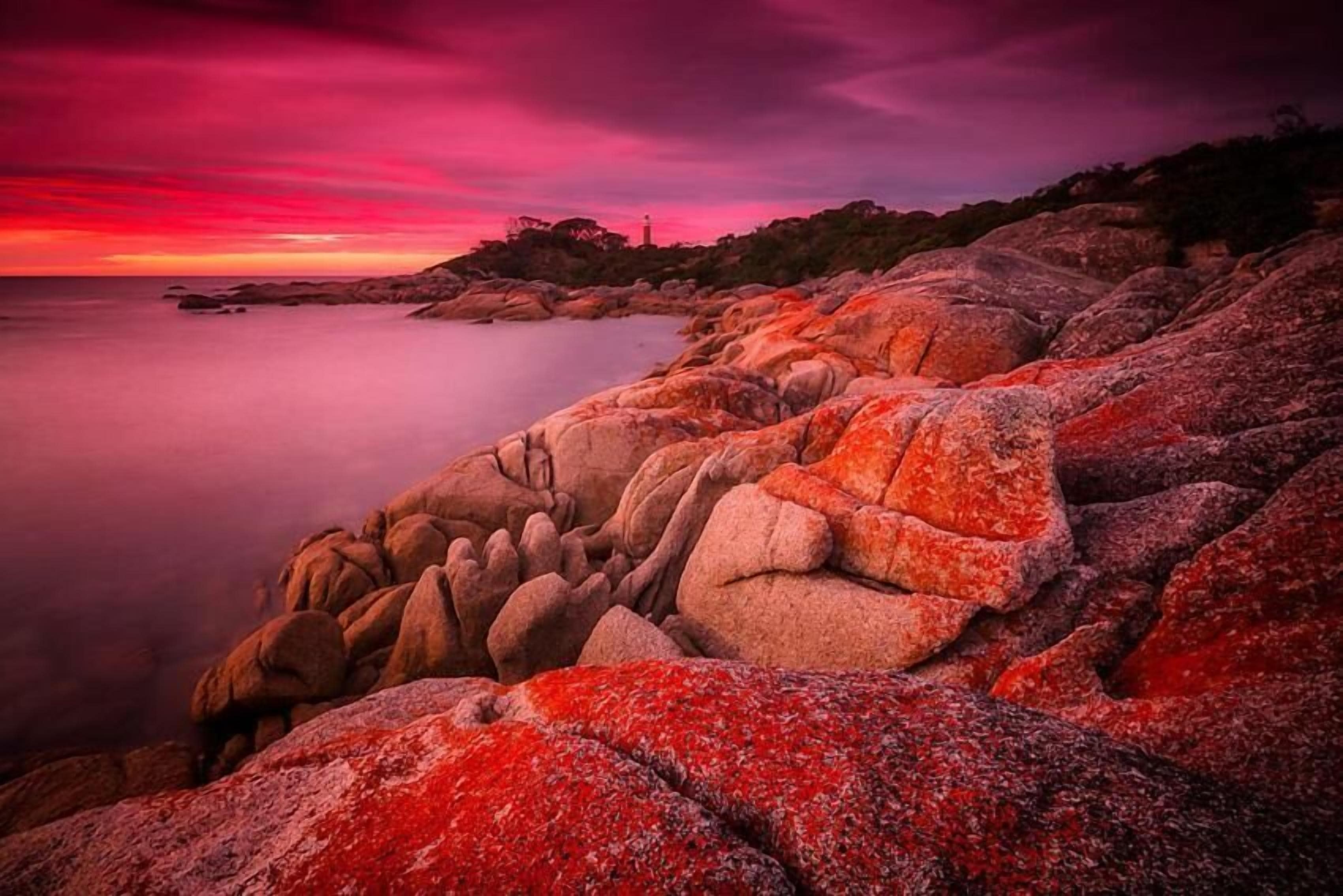 A coastal landscape with large rocks and a lighthouse in the distance.