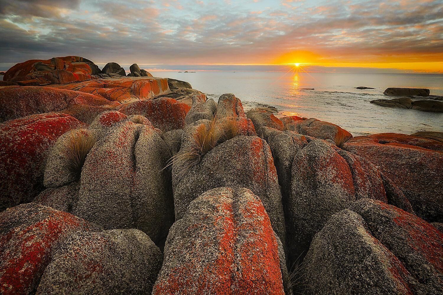 A rocky shoreline with large boulders and a sunset in the background.