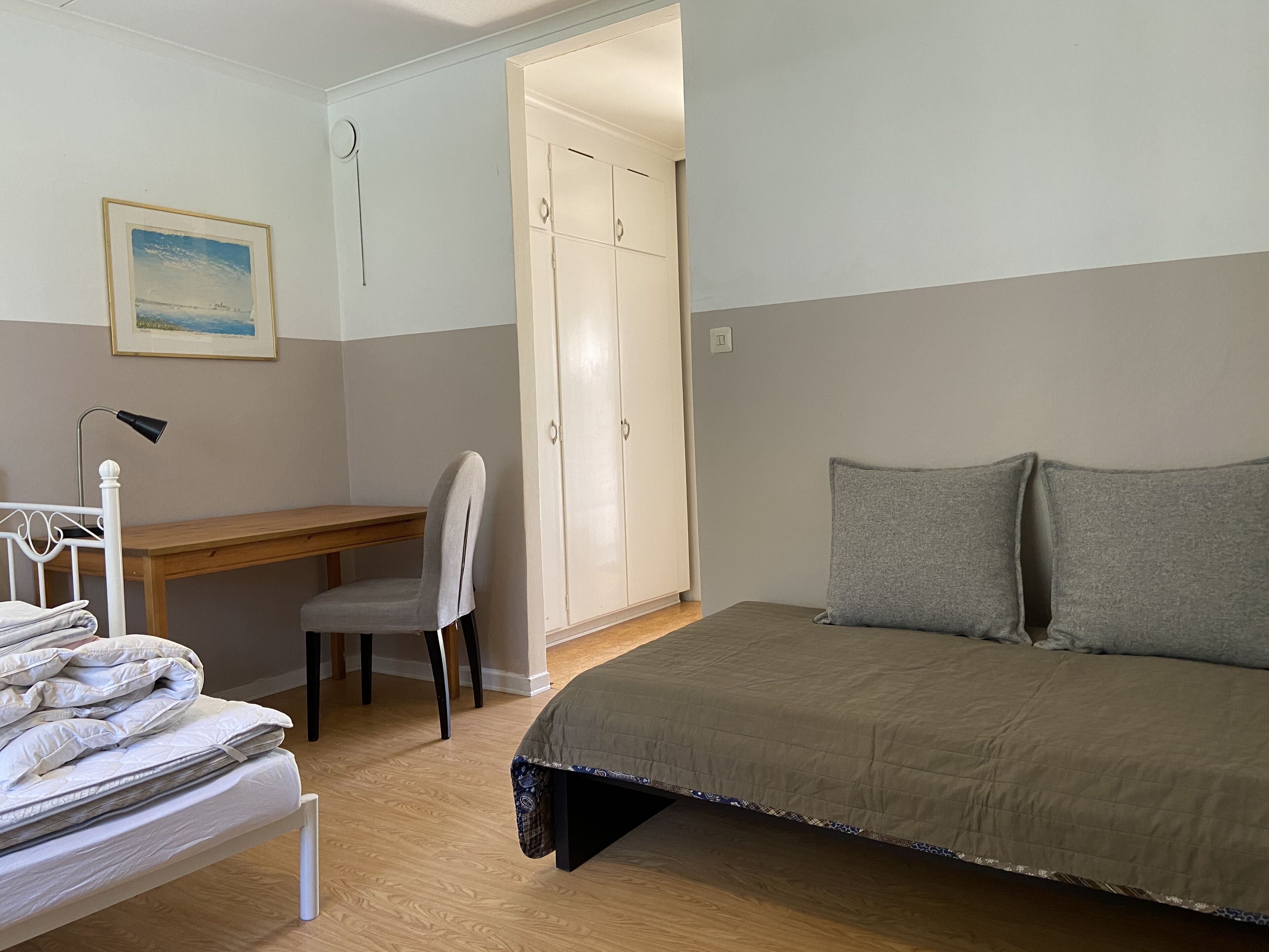 A bedroom with a bed, a desk, a chair, a wardrobe, and a bedside table.