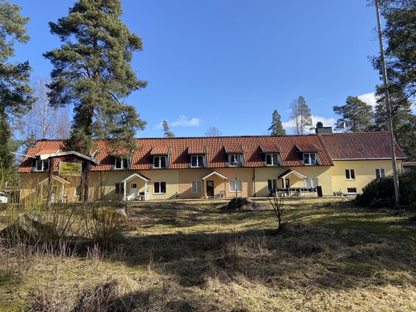 A two-story building with a red-tiled roof, multiple windows, and a small porch area. - Garpgården (Garpenberg)