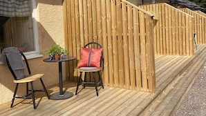 Une terrasse en bois avec une chaise et une table, une clôture en bois et un bâtiment doté d’une fenêtre.