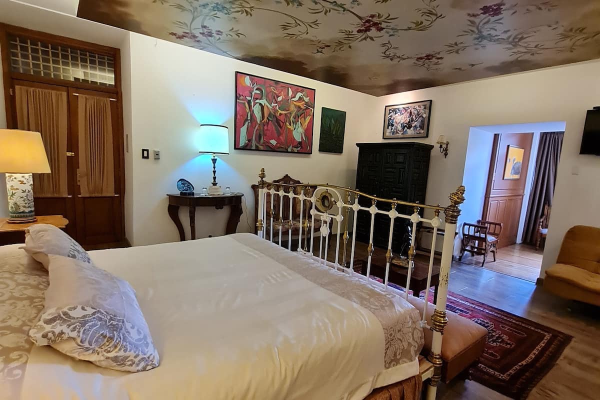 A bedroom with a bed, a wooden headboard, a ceiling with floral patterns, and a painting on the wall.