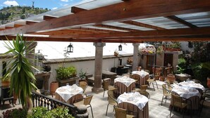 Eine Terrassengruppe mit Esstischen, umgeben von Kübelpflanzen und einer Pergola.