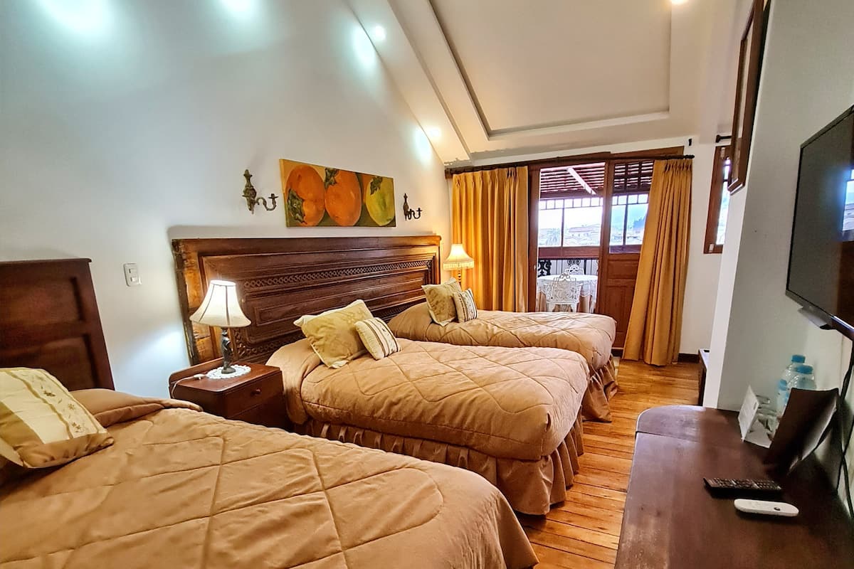 A hotel room with three beds, wooden flooring, a TV, and a table with a remote control.