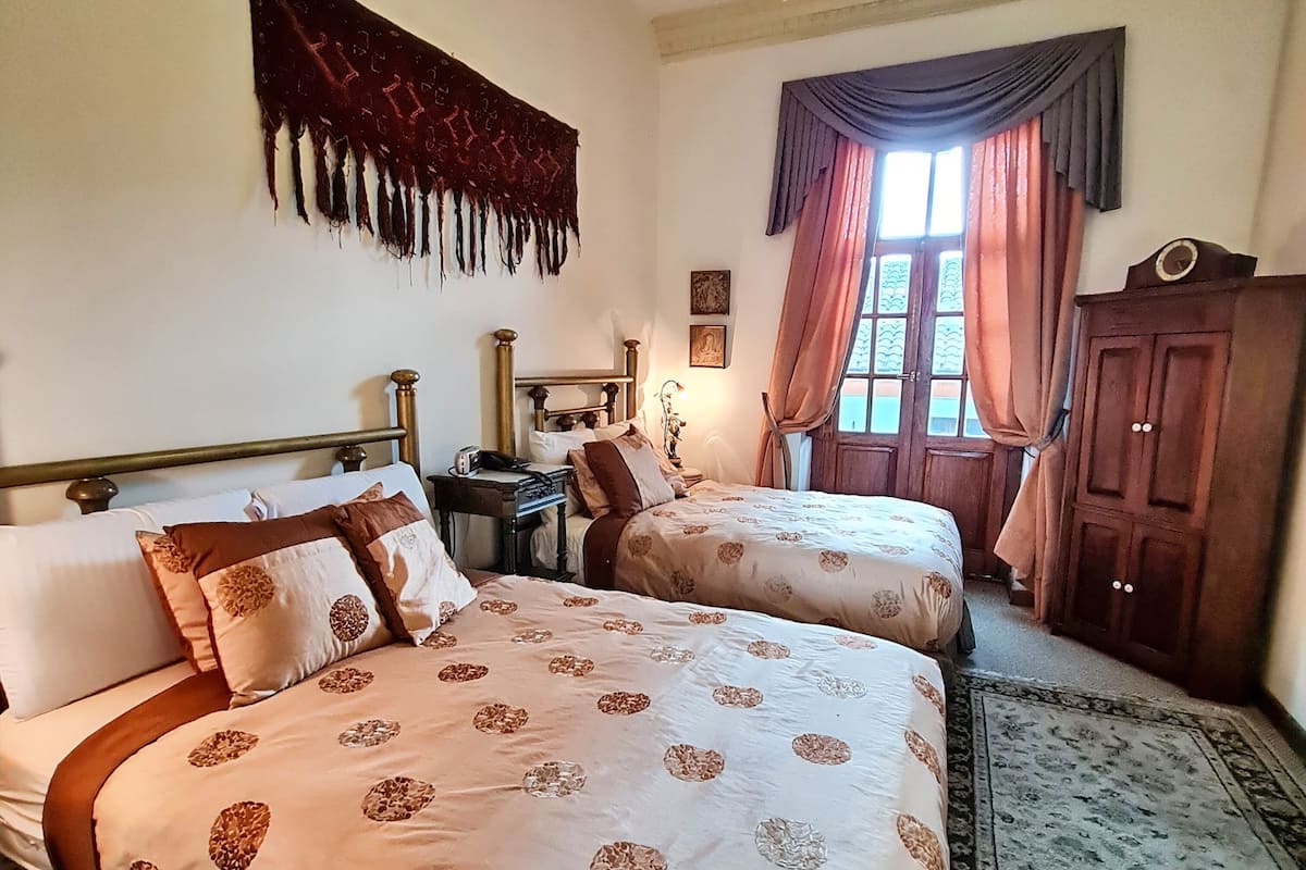 A room with two beds, a wooden wardrobe, a chandelier, and a window with curtains.