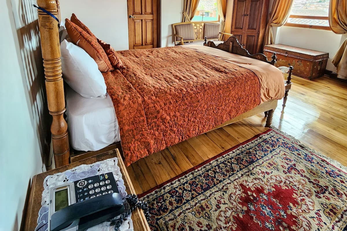 A bedroom with a wooden bed, a bedside table with a telephone, a wooden wardrobe, a television, and a window with curtains.
