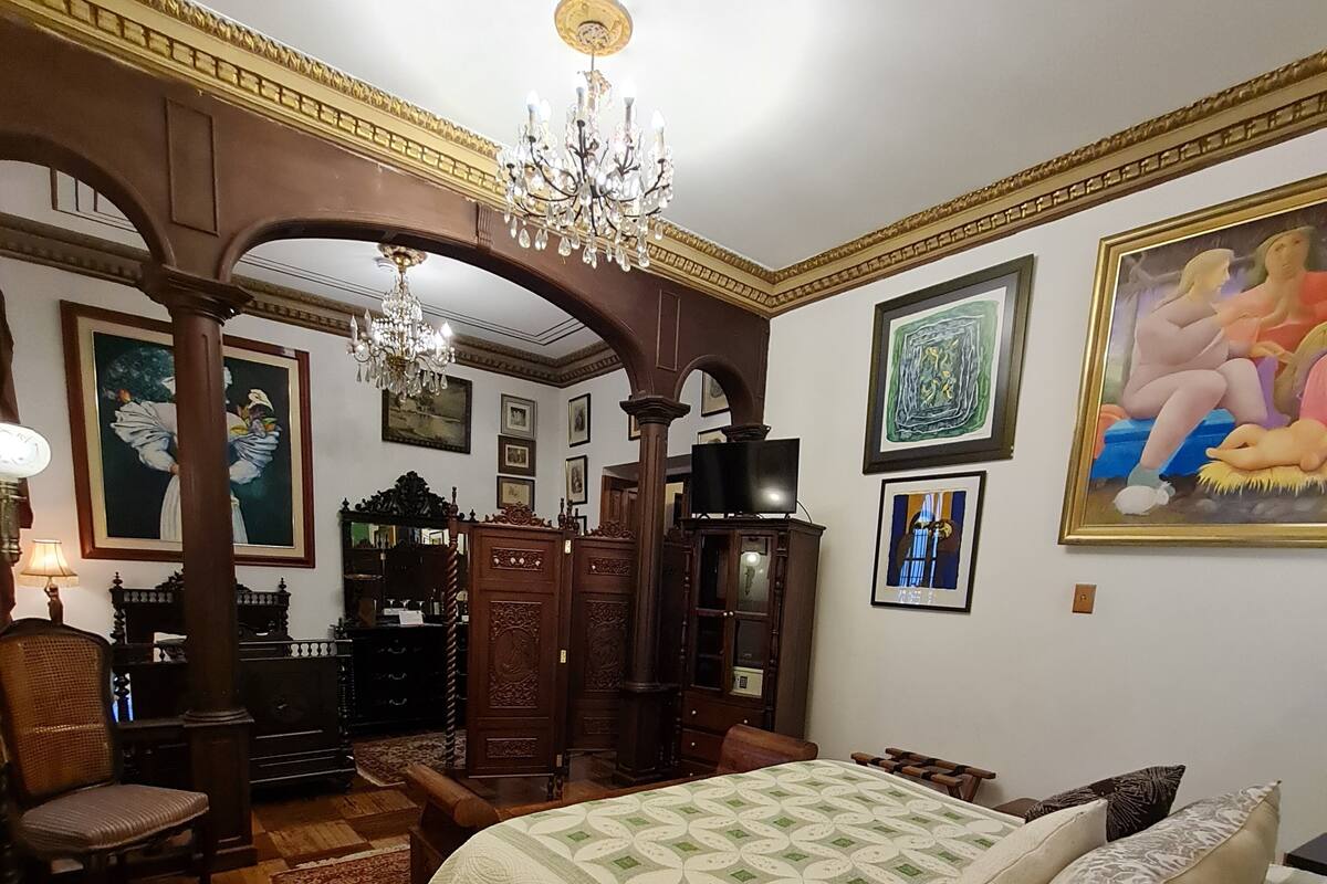 A room with a large bed, wooden furniture, a chandelier, and artwork on the walls.