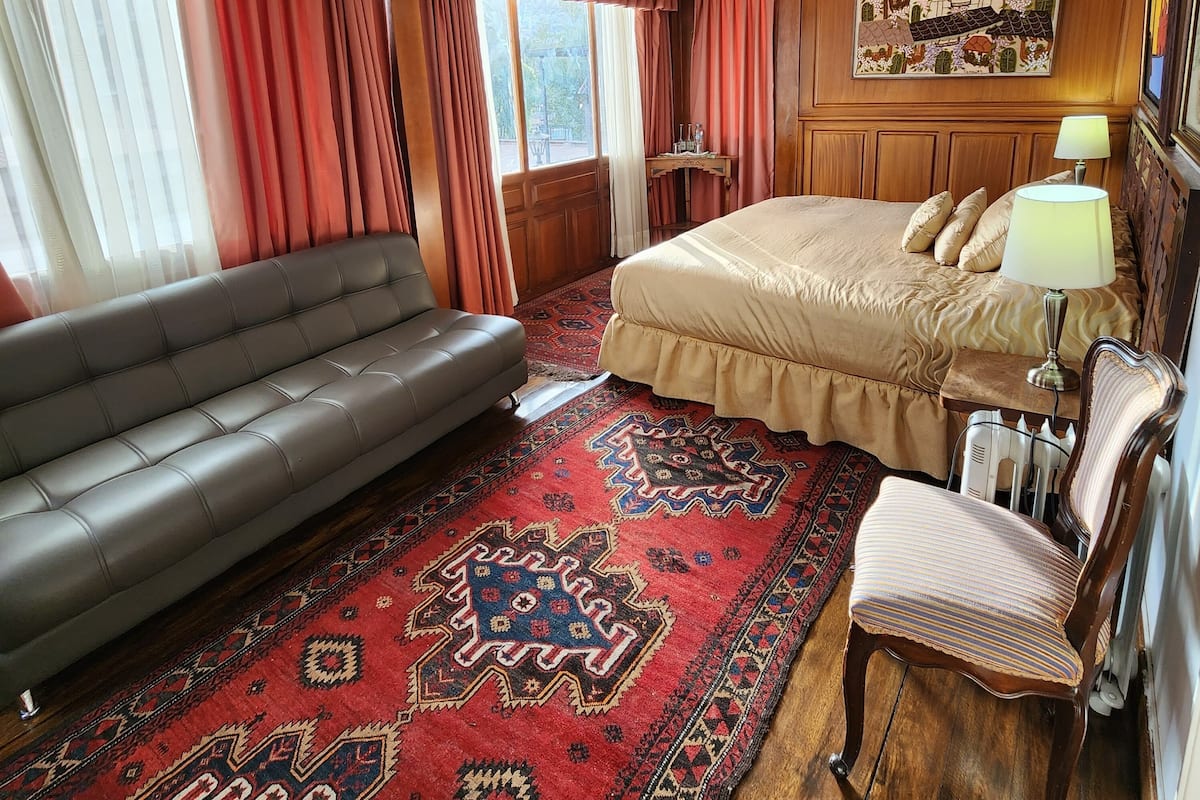 A hotel room with a bed, a sofa, a chair, a rug, and a chandelier.