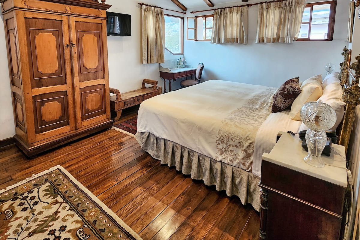 A bedroom with a large bed, wooden wardrobe, and a television on the wall.