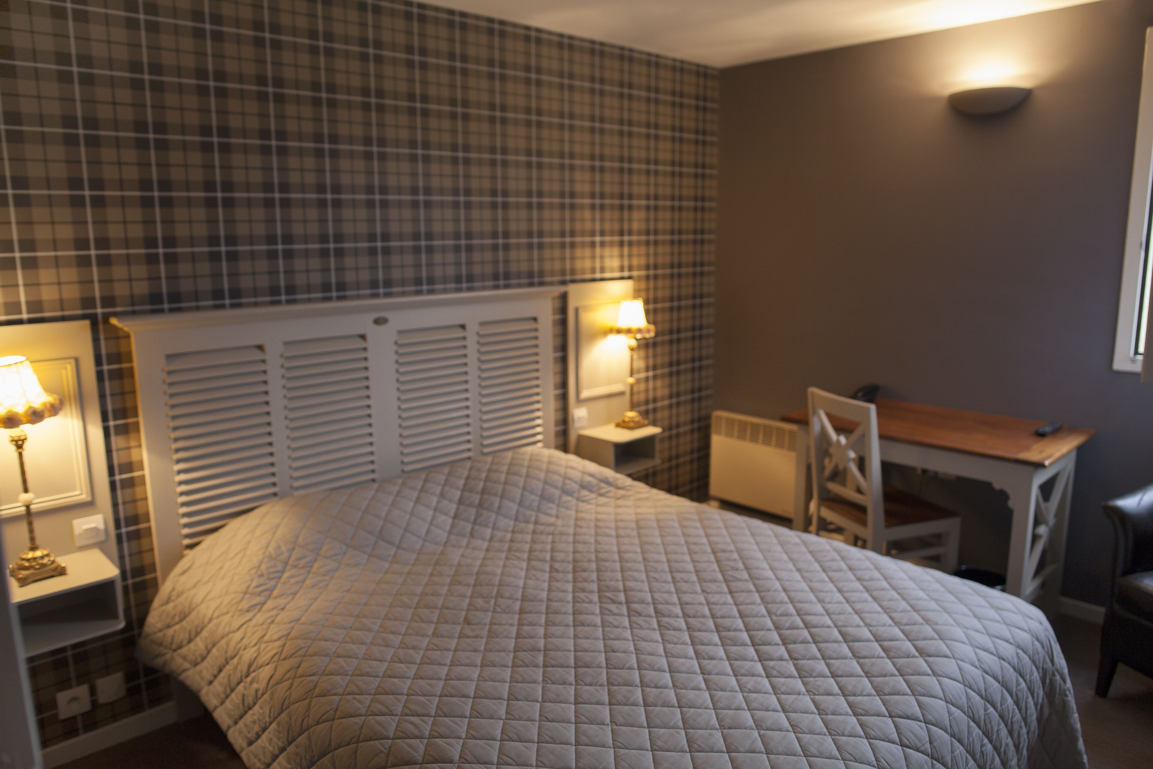 Une chambre à coucher comprenant un lit, deux tables de chevet avec des lampes, un bureau et une chaise.