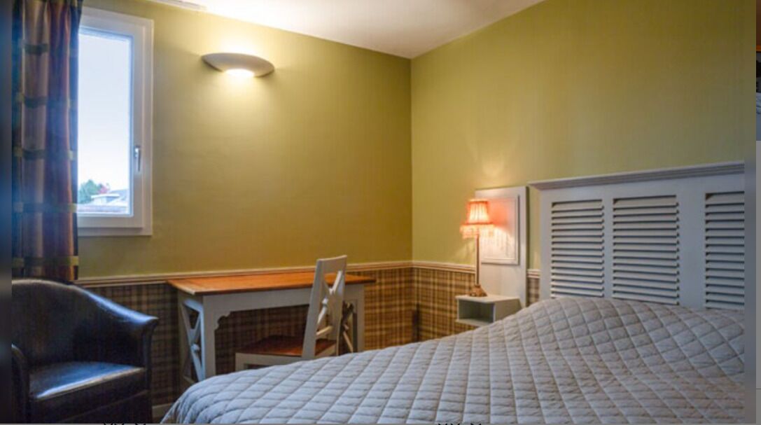 Een slaapkamer met een bed, een bureau, een stoel, een raam en een wandlamp.