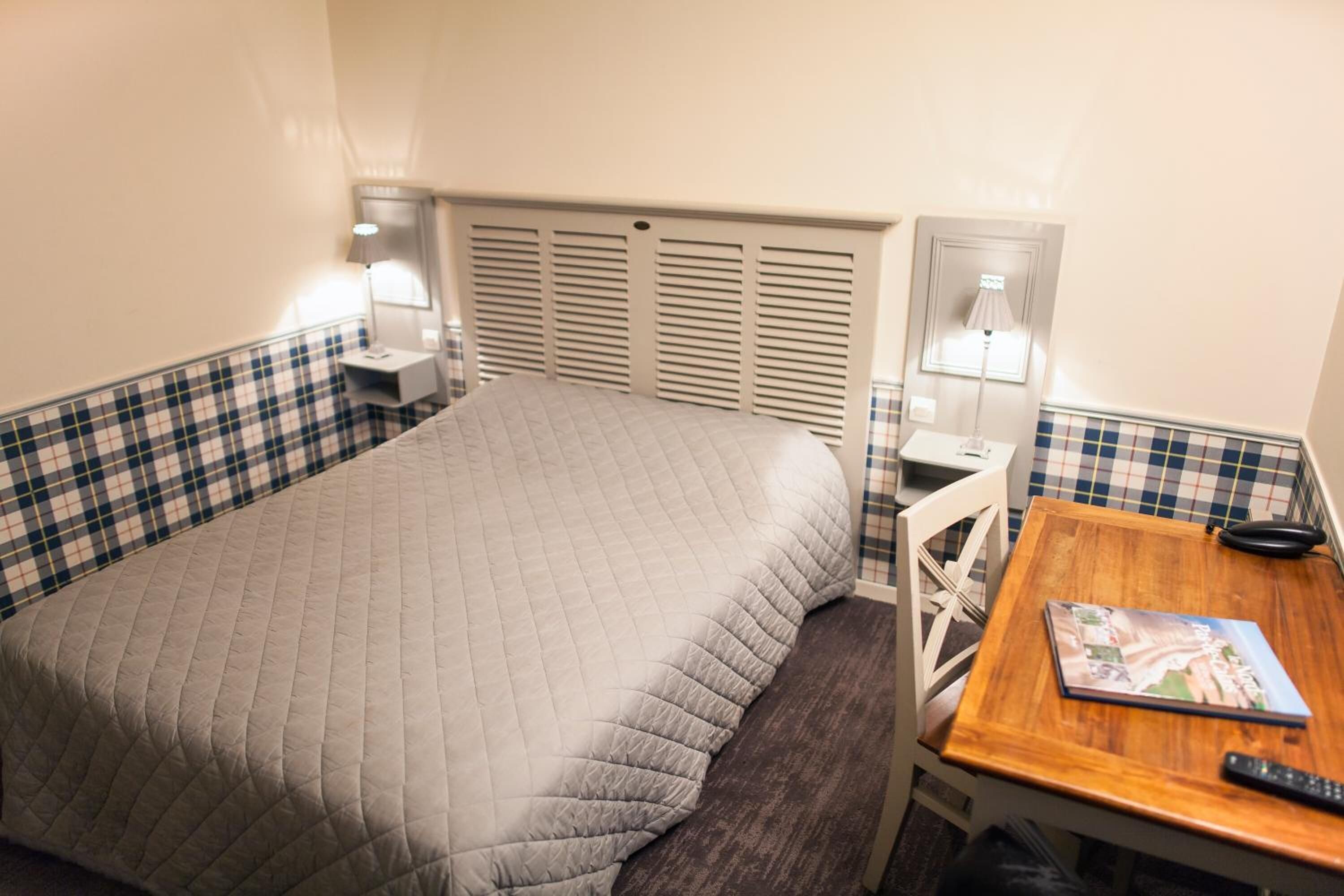 Hotelkamer met een bed, een bureau en een stoel. Twee bedlampen en een raam met jaloezieën.