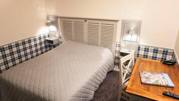 Une chambre d’hôtel avec un lit, un bureau et une chaise. Il y a deux lampes de chevet et une fenêtre avec des stores.