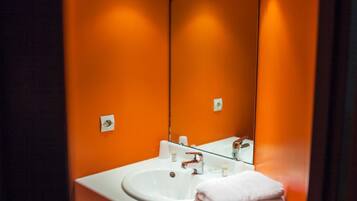 Un baño con una pared naranja, un lavamanos blanco y un espejo.