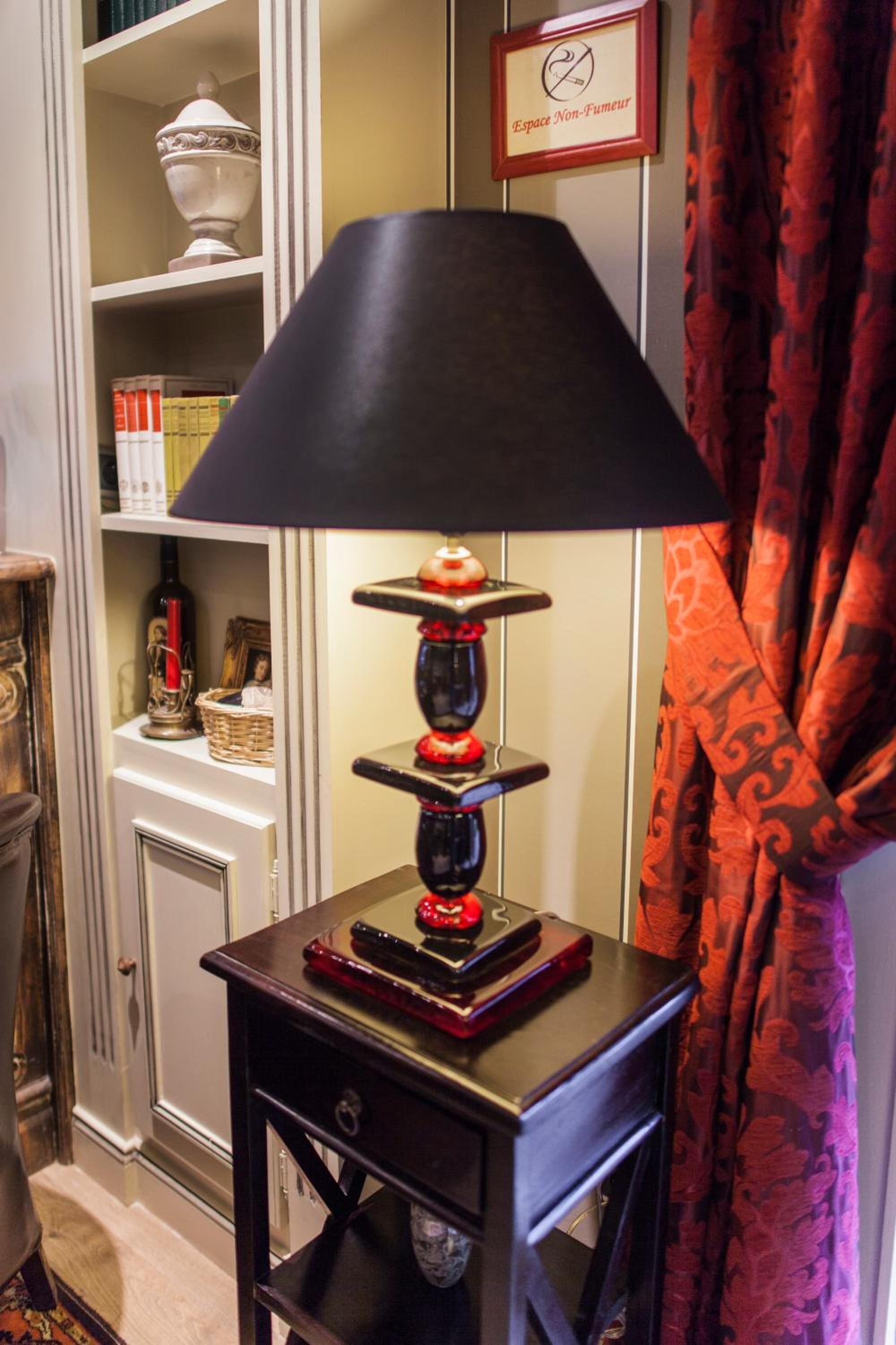Een tafel met een zwarte lamp, een decoratief object en een klein plankje met boeken en een fles.