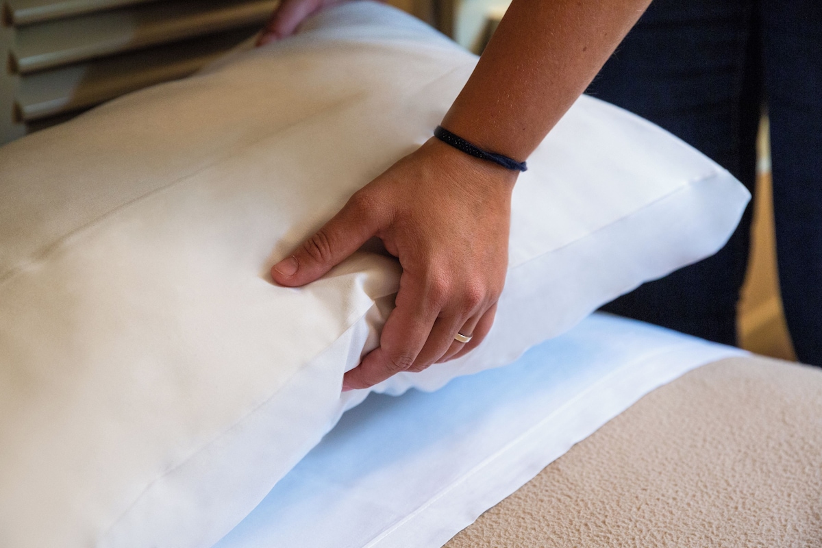 Une main ajuste un oreiller blanc sur un lit.