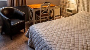 Een hotelkamer met een bed, bureau, stoel en lamp.